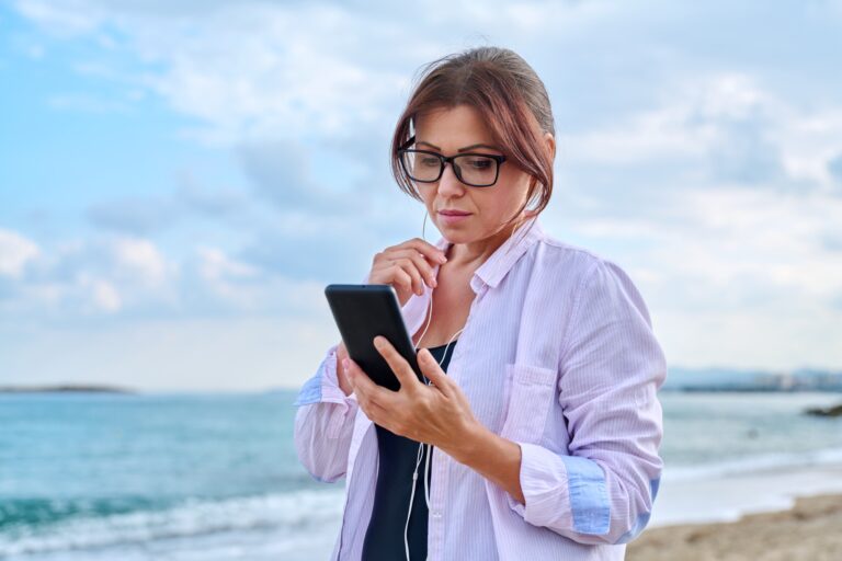 Middle age sad serious woman in headphones with smartphone outdoor.